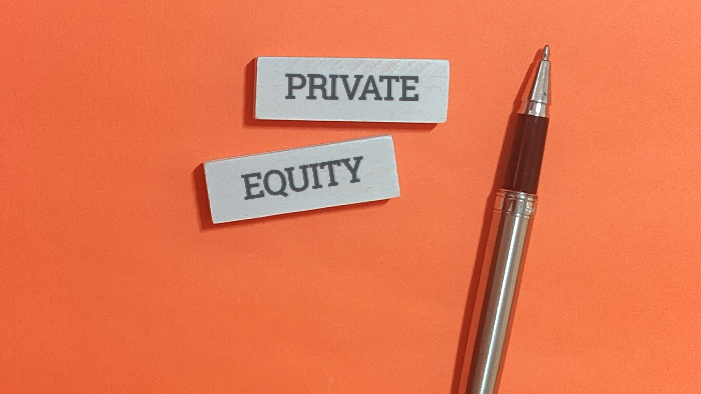 the words "private equity" written out on gray paper next to a pen with a bright orange background