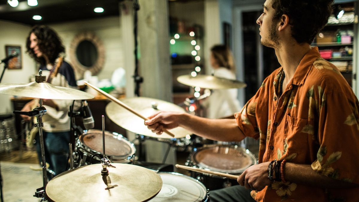 Man wearing orange shirt plays drums