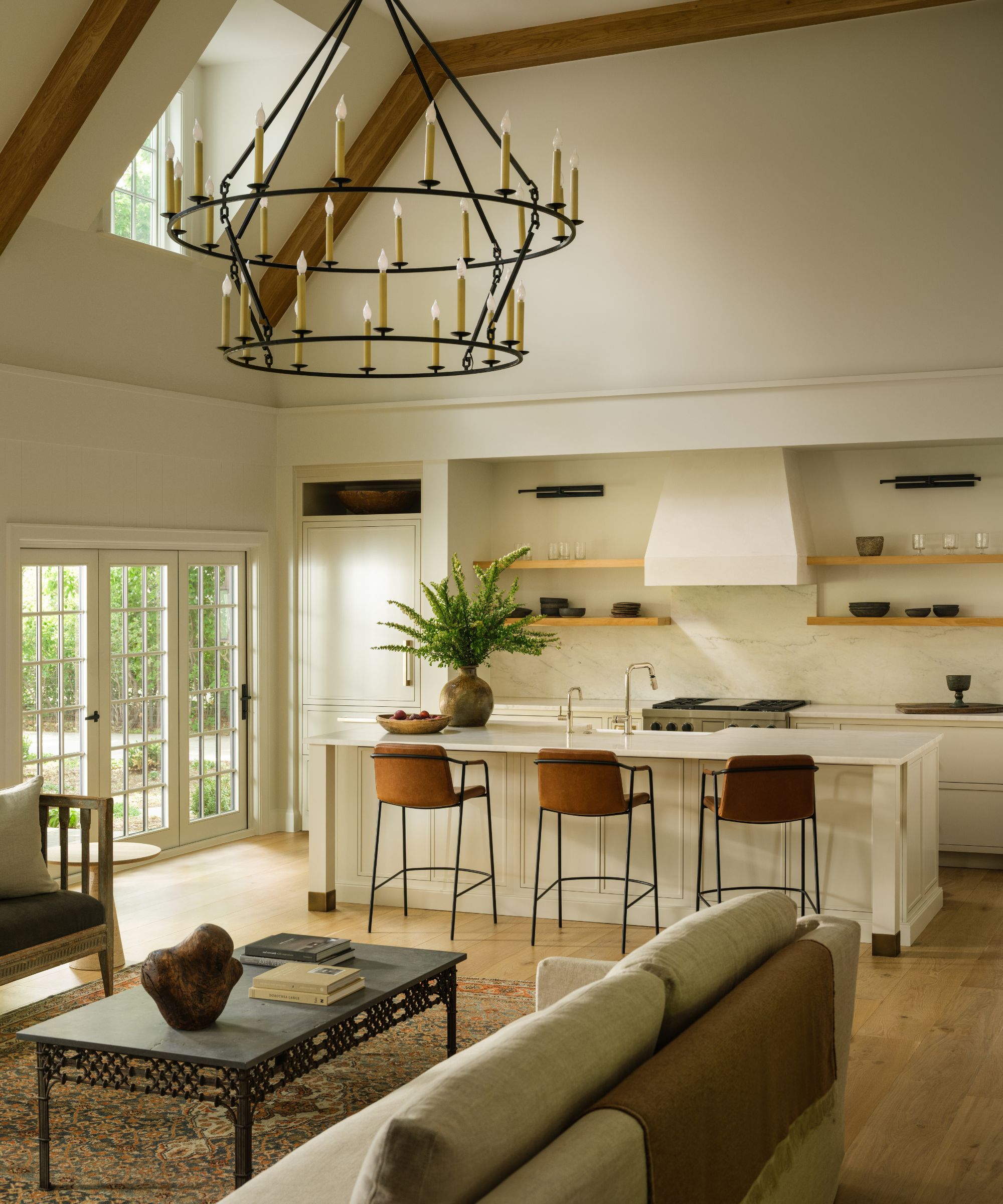 a large pale cream great room with a modern white kitchen, vaulted beamed ceiling, a living area with an iron chandelier and vintage style furnishings