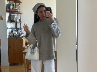 Woman takes a mirror selfie in a head scarf, taupe sweater, white jeans, white Longchamp purse and black patent leather shoes.
