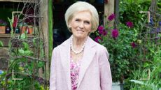 Mary Berry in a pink floral dress and pink coat in a garden