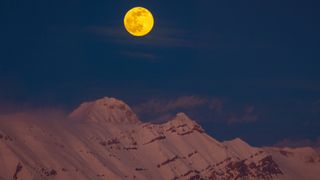 a bright full moon above a snowy mountain range