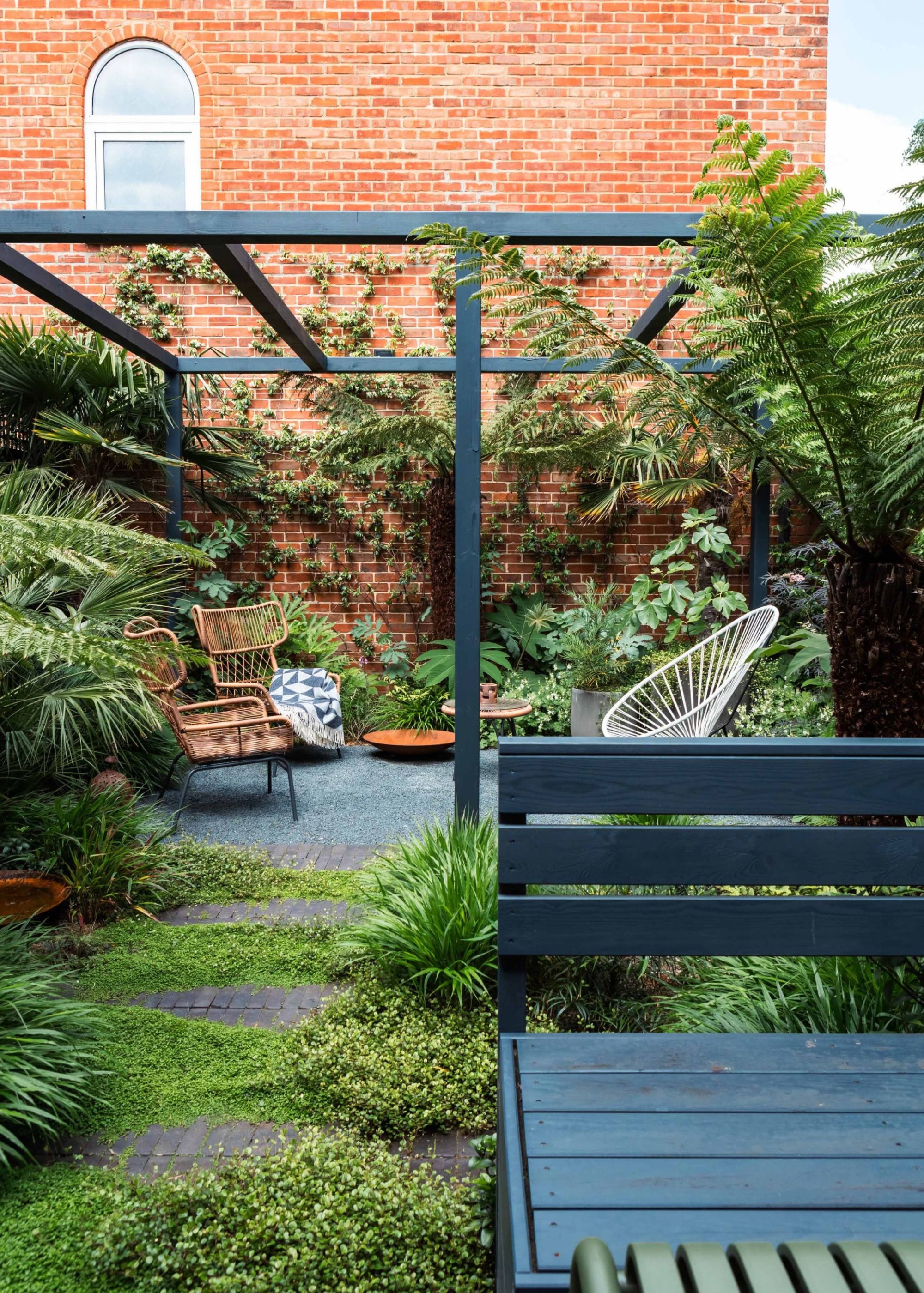 A calming red-brick-walled urban garden with repeated immersive planting and a pergola by GRDN, with a bench in the same color as the pergola at the front