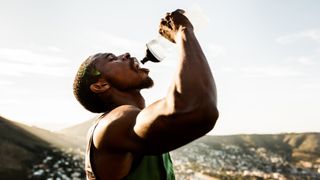 A man in athletic apparel squeezes water into his mouth from a water bottle