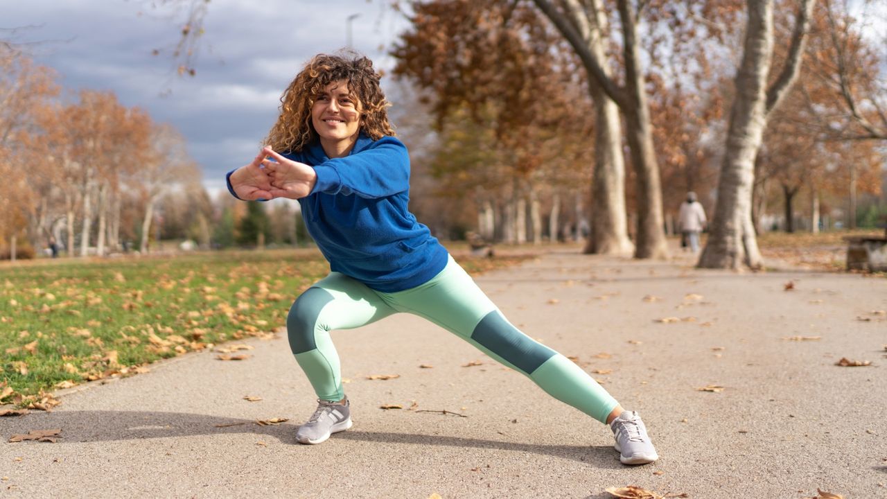 woman in the park doing a side lunge wearing mint green legging and blue long sleeved top.