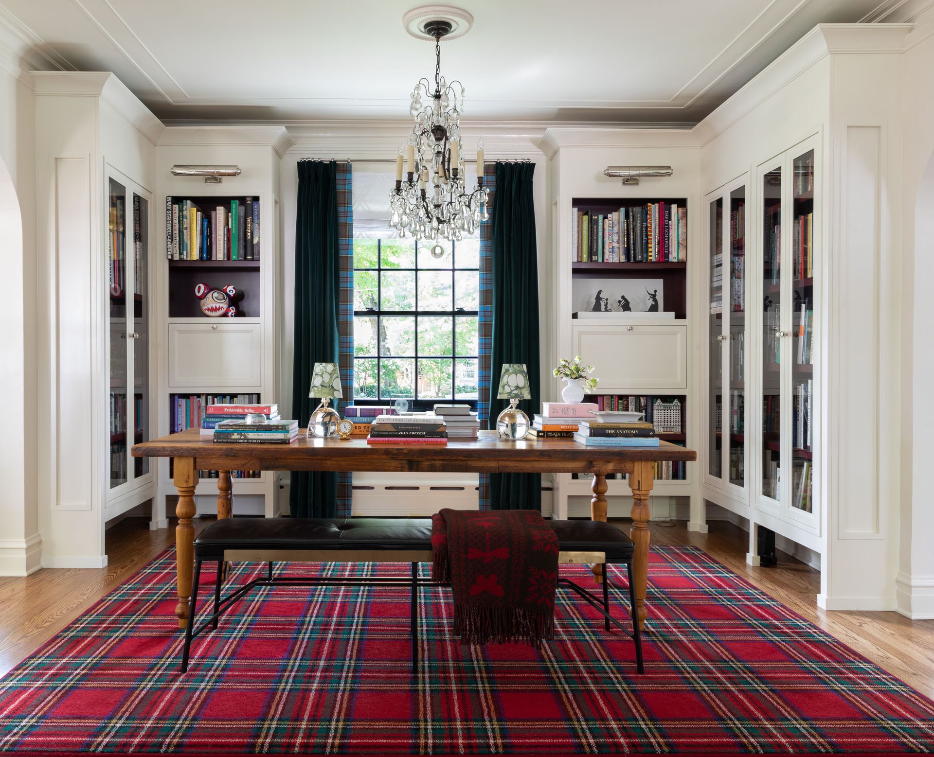Study with shelving built in to corners, table and bench seating, chandelier, wood floor, tartan rug in read and tartan curtains in blue