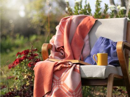 A cozy blanket and mug on a chair outdors