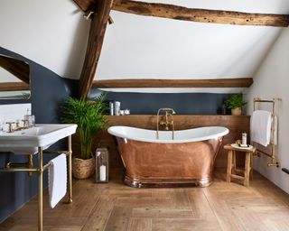 Large bathroom with copper bathtub, navy and white paint ideas, wooden flooring, plants and candles, beamed ceiling