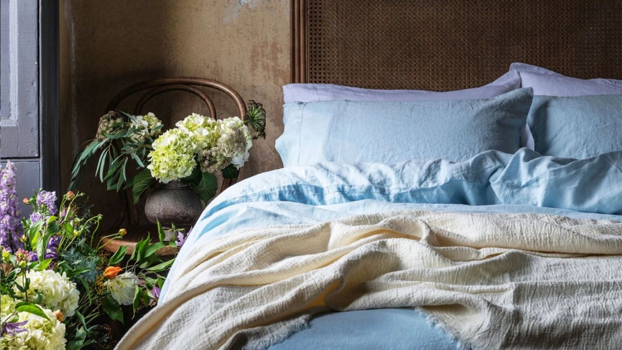 Blue sheets on a bed against a wooden wall beside potted flowers.