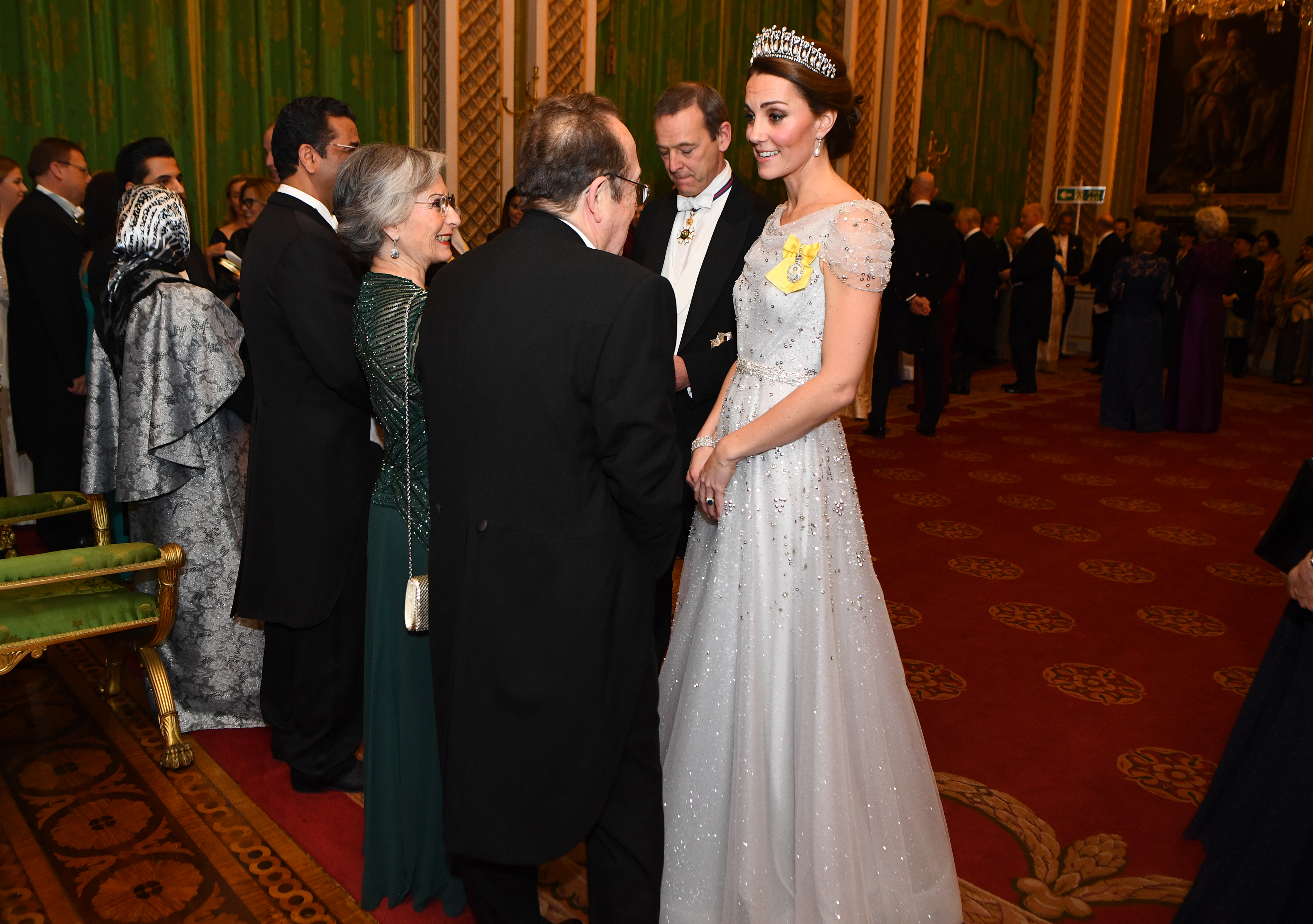 Kate Middleton wearing a white gown and tiara talking to a man at a palace reception