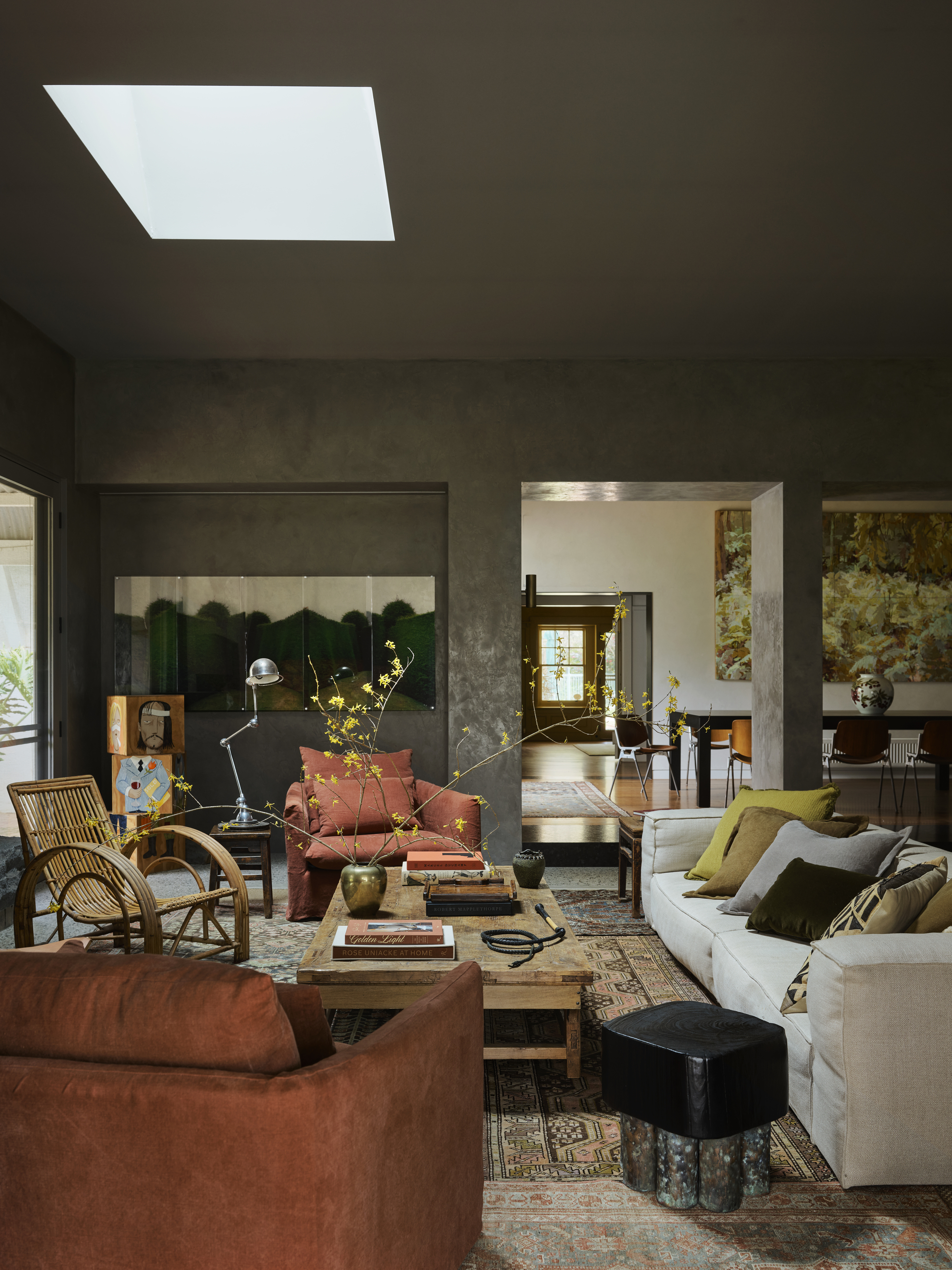cozy living room with textured walls, large artwork, white sofa with colorful cushions, timber table styled with vase of large stems and coffee table books, rattan armchair, rust linen armchair, side table with silver table lamp