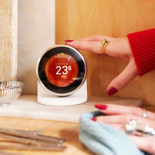 A woman reaching out to a smart home thermostat