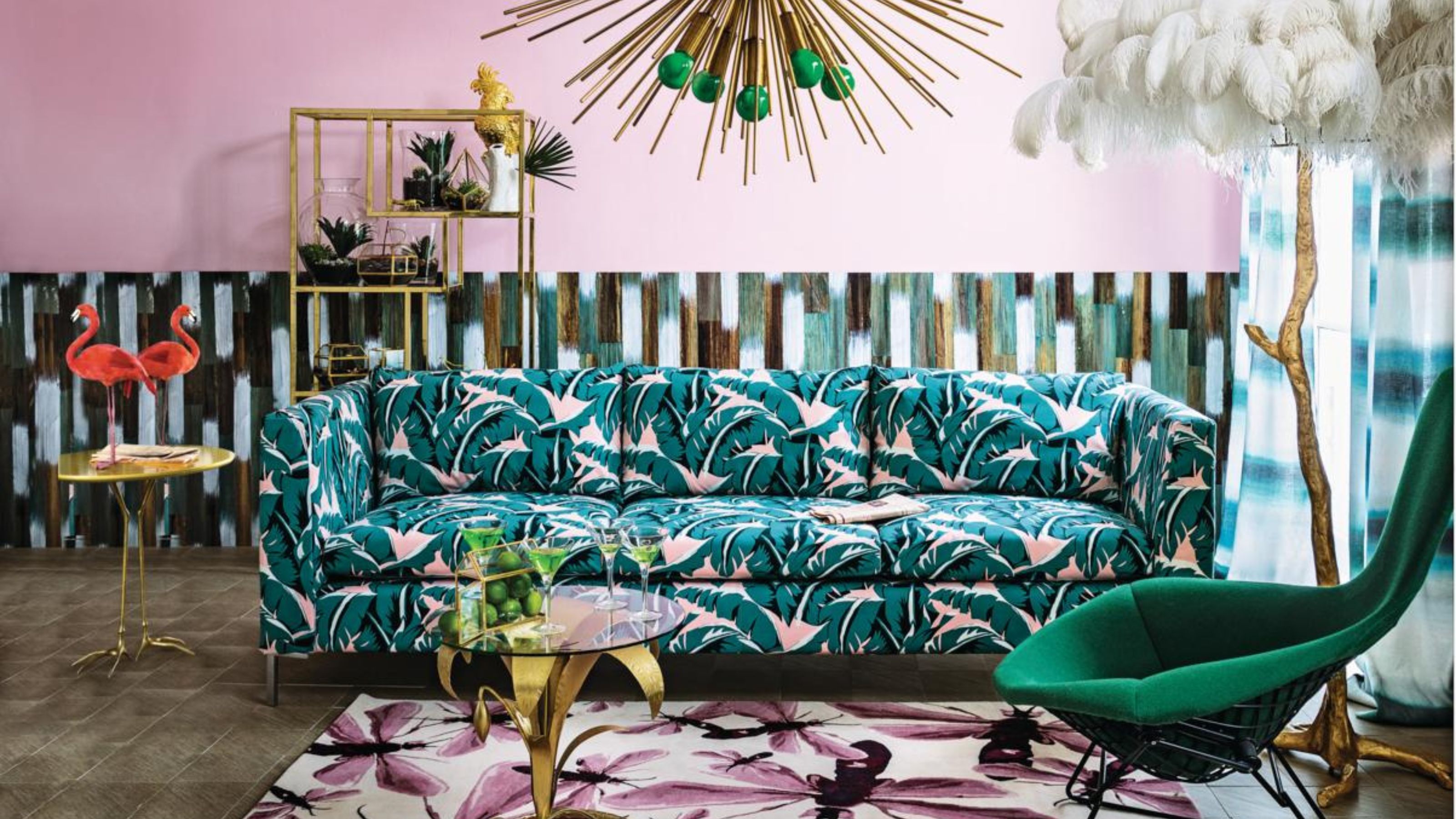 A maximalist living room painted bubble gum pink with different patterns all around the room. There is a tropical print sofa, a dragonfly rug, and tie-dye curtains.