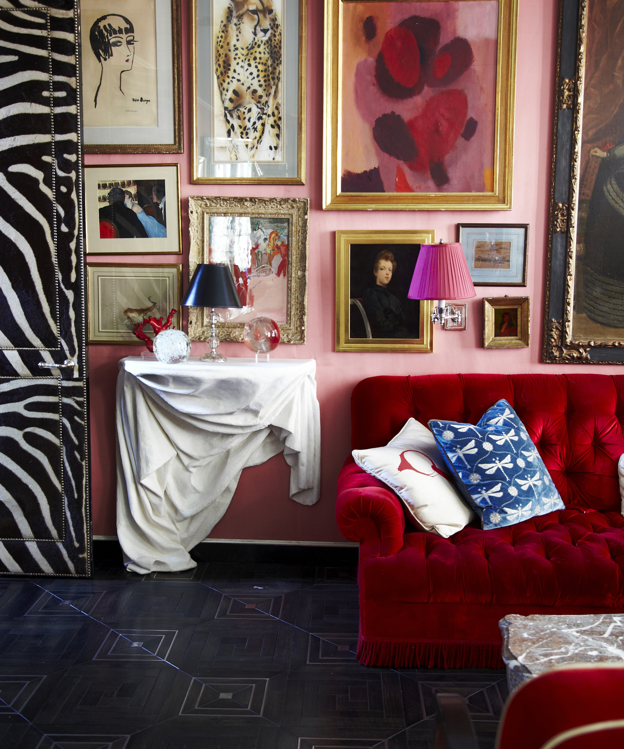 maximalist living room with pink wall, red sofa and a lot of art hung on the wall