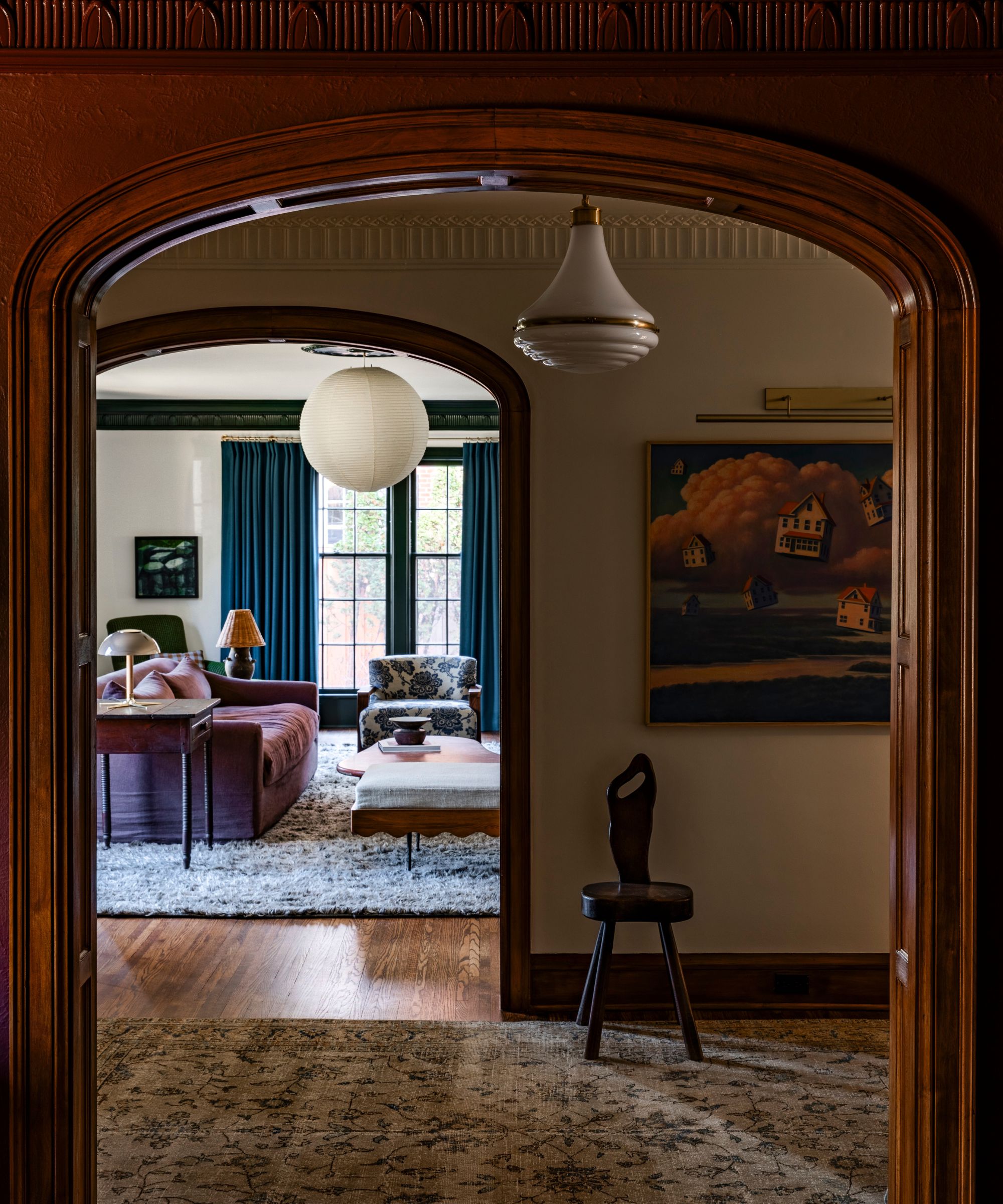 Grand hallway with arched doorways leading into the living room. A vintage glass flush-mount hangs from the ceiling, and a rustic stool sits beneath a large vintage landscape painting.