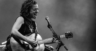 A black and white image of Ani DiFranco playing live with an acoustic