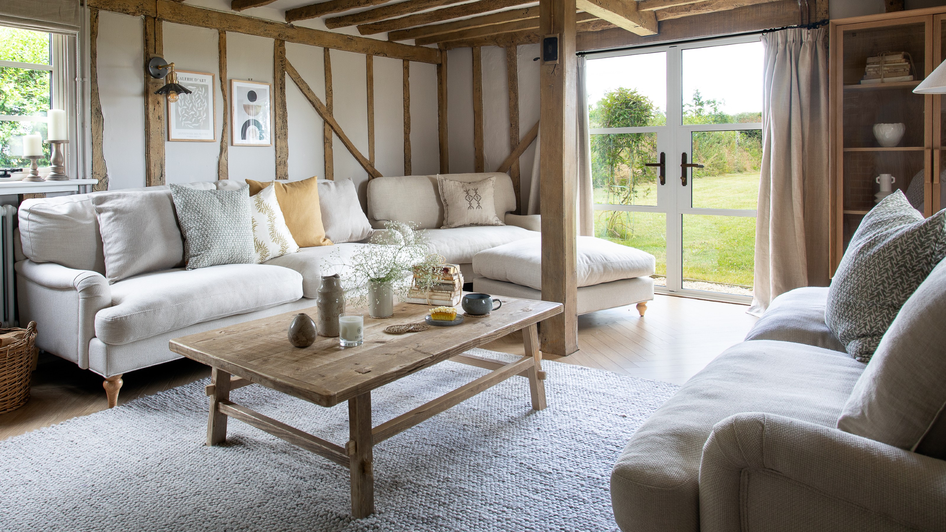 A neutral living room with beams, a beige sofa and tonal curtains