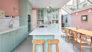 large kitchen with pale green units and pink walls