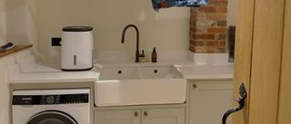The MeacoDry Arete One 6L Compact dehumidifier on a worktop in a utility room with an oak door and double sink visible
