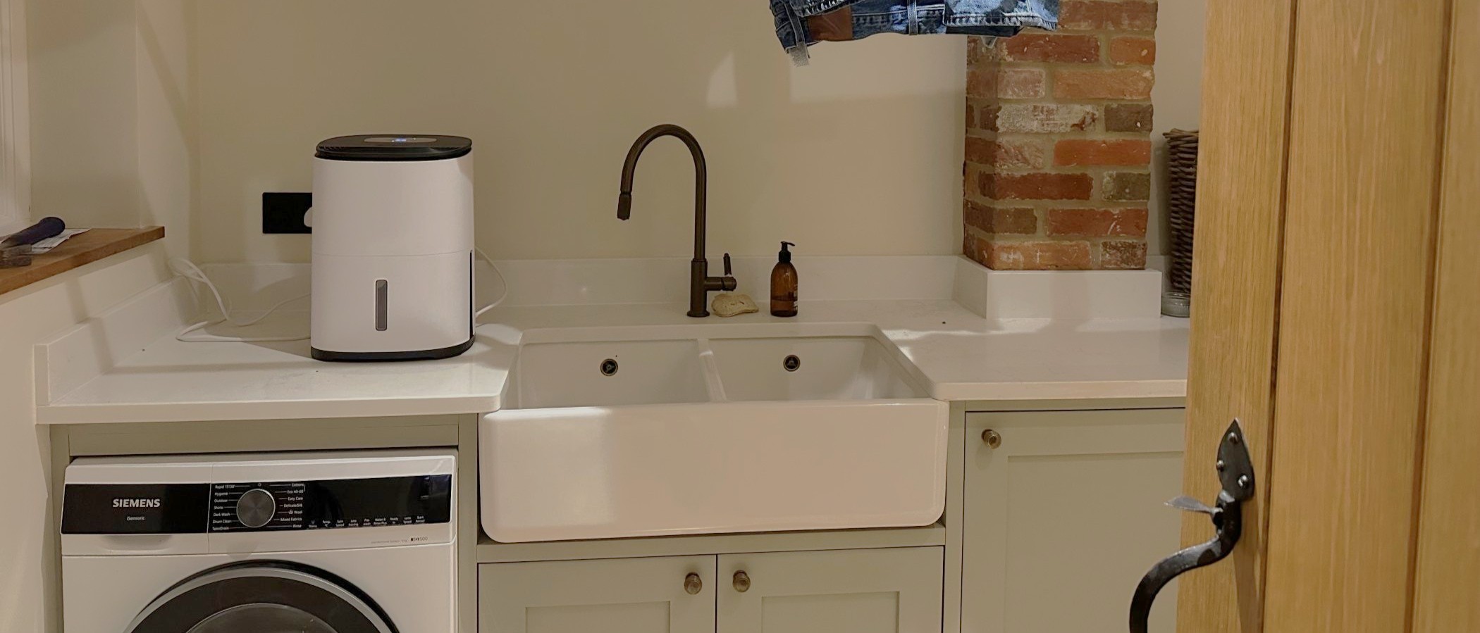 The MeacoDry Arete One 6L Compact dehumidifier on a worktop in a utility room with an oak door and double sink visible