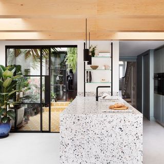 White kitchen with a terrazzo kitchen island and view into a sun room winter garden