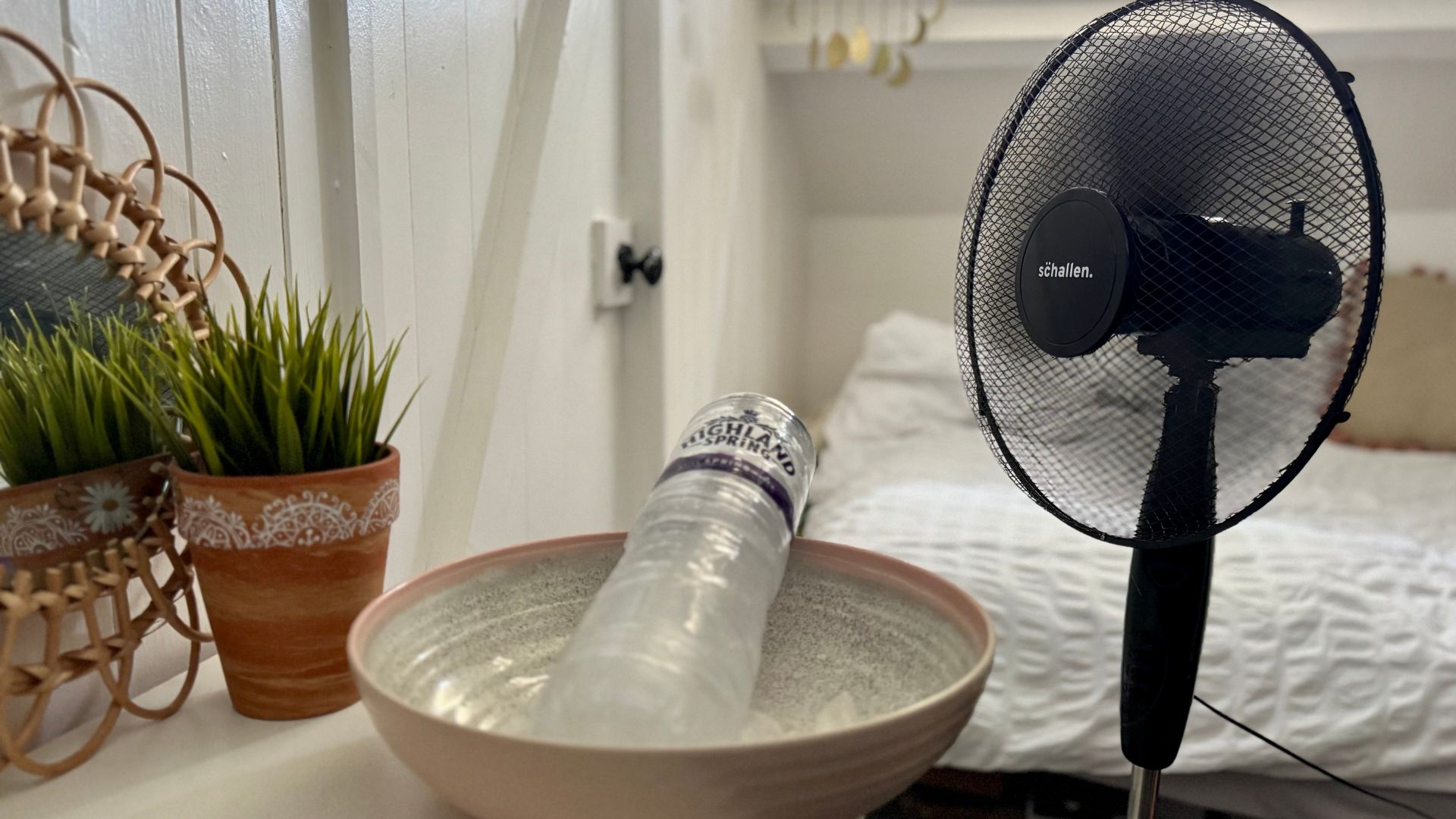 A black fan next to bowl holding a bottle of ice representing DIY air con hack