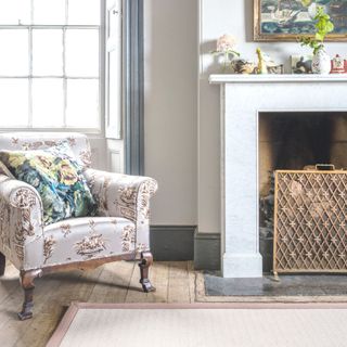 grey armchair in living room with white walls and grey skirting board neutral rug in centre of room in front of marble fireplace