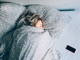 girl sleeping in bed with ikea floral bedding and phone beside her by getty images