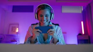 A young woman wearing headphones and playing a game on her mobile phone.