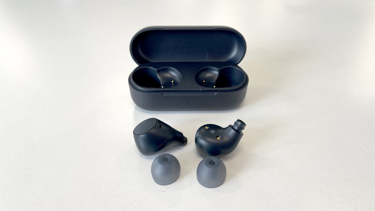 A black pair of Sony WF-C510 in-ear headphones out of the case with the ear tips removed. The case is in the background with the lid open. They are on a white background.