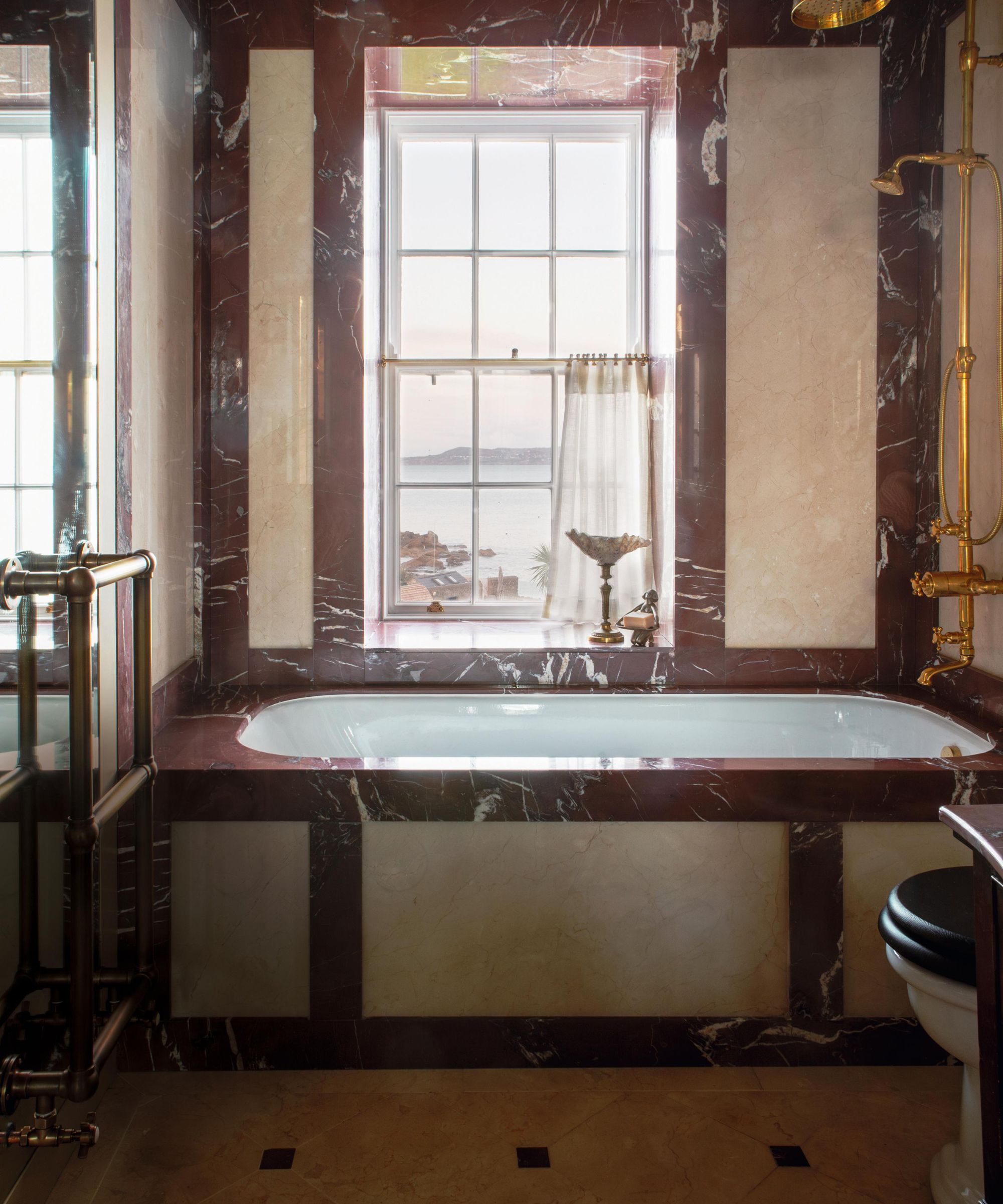 a red marbled bathroom with built in bathtub and bright brass shower mixer