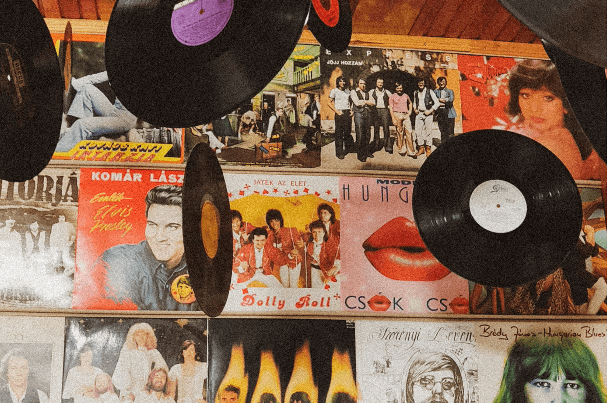 A close-up shot shows several vinyl records hanging in front of a wall covered with vintage album covers.