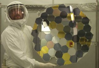 a scientist in a clean suit holds up a large disc covered in metallic hexagons