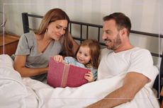parents in bed with daughter reading book