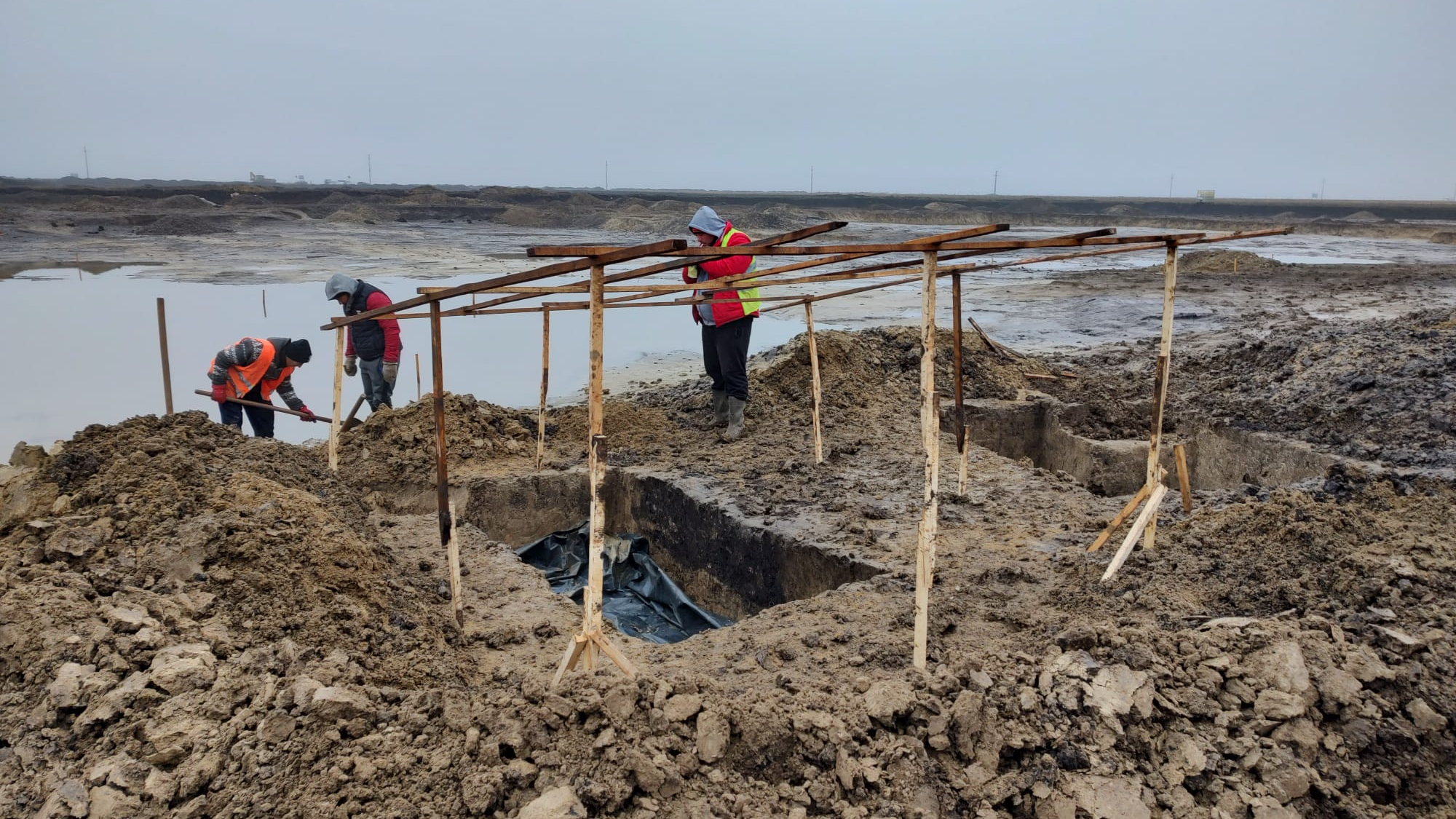 Three workers dig on a dirt- and snow-covered landscape, where they found found a warrior's burial in Romania.