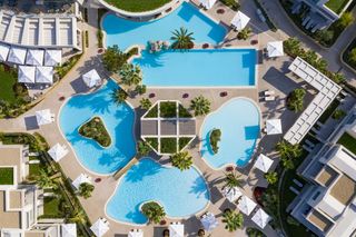 An aerial shot of some of the lagoon shaped pools at Porto Sani, which are landscaped with palm trees and are surrounded by loungers