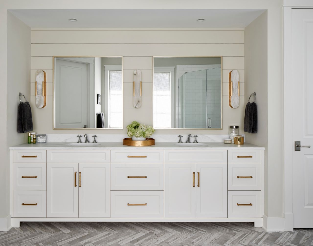 white bathroom with white cladding, white cabinetry, two mirrors and gray parquet style flooring