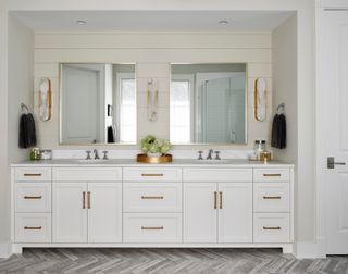 white bathroom with white cladding, white cabinetry, two mirrors and gray parquet style flooring