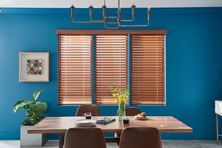Wooden blinds in blue dining room with wooden table and wall art