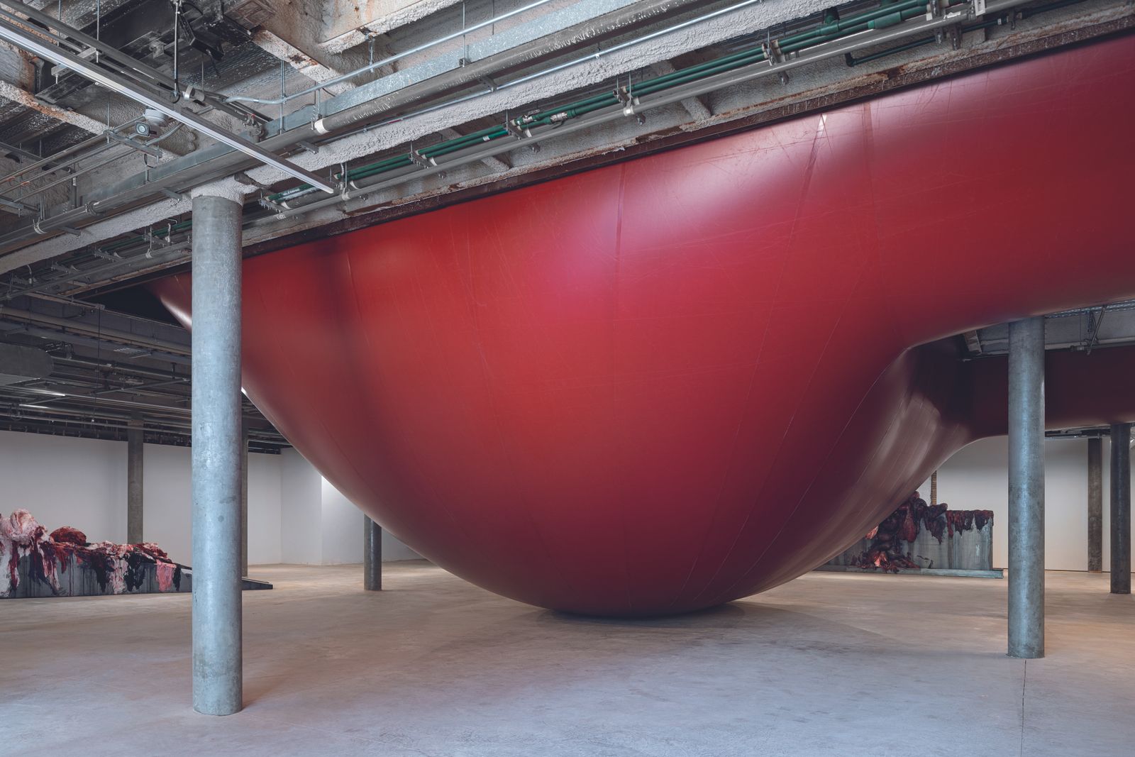 Vast red bulbous sculpture within concrete space