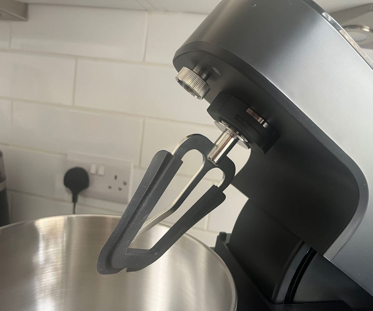 A close up of a beater paddle attachment on a black stand mixer with its head tilted back