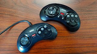 Retro-bit 8-Button Arcade Pad next to original Sega Mega Drive (Genesis) controller on woodgrain desk