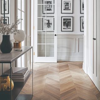 A bright white hallway with a gallery wall display and a console table with a marble top displaying decorative items