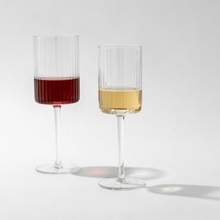 two ridged flat bottom wine glasses, one with white wine and one with red wine inside
