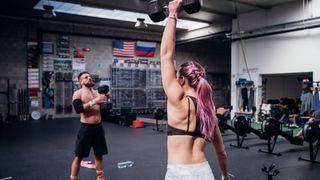 Woman and man perform dumbbell snatches in gym