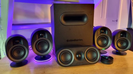 The SteelSeries Arena 9 illuminated 5.1 desktop speakers, lit up in purple on a wooden dining room table