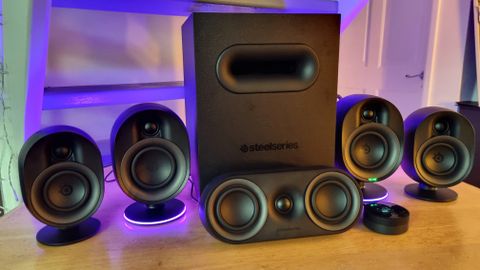 The SteelSeries Arena 9 illuminated 5.1 desktop speakers, lit up in purple on a wooden dining room table