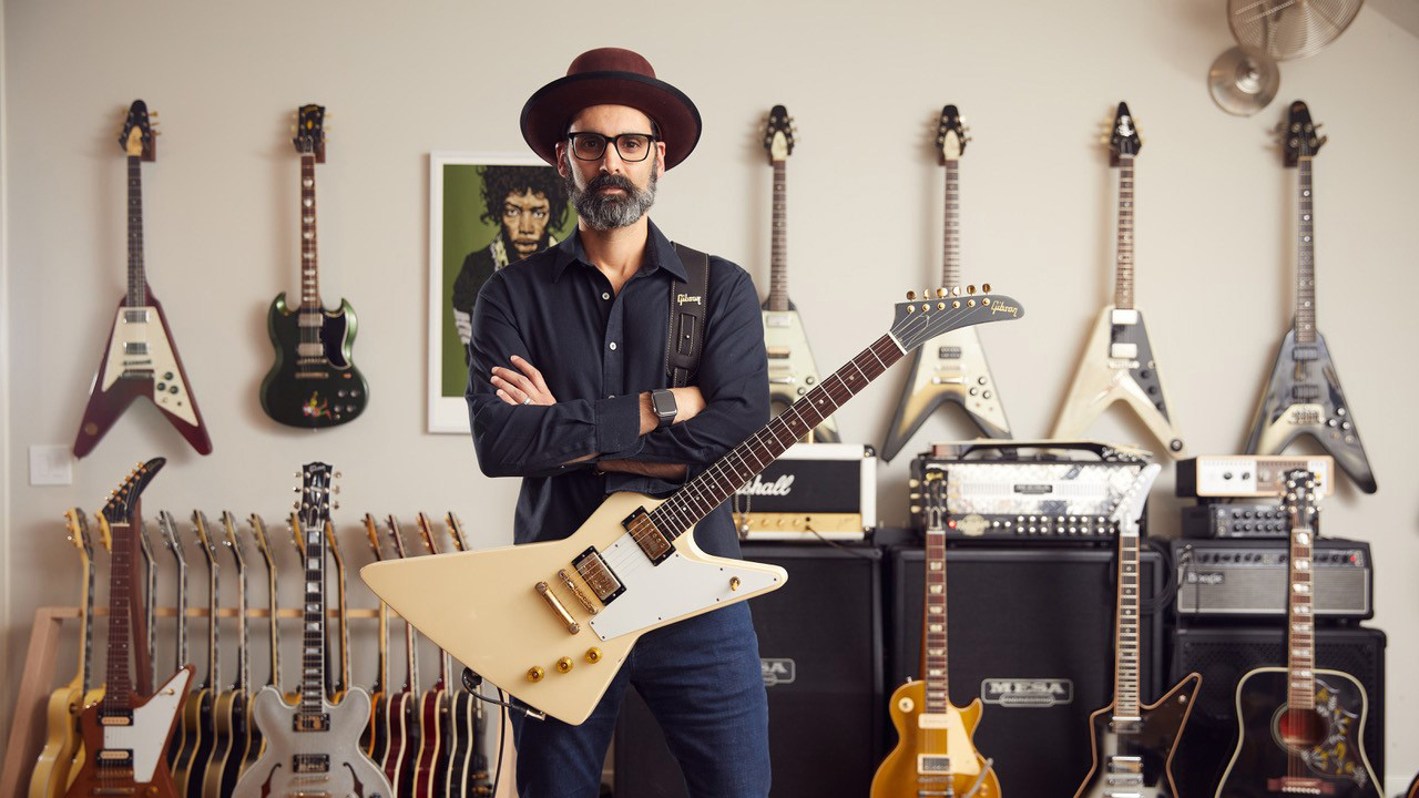Cesar Gueikian poses with a Gibson Explorer in front of a wall of Gibson guitars