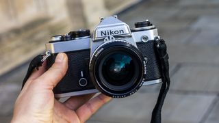 The Nikon Fe held by a photographer in front of a pavement