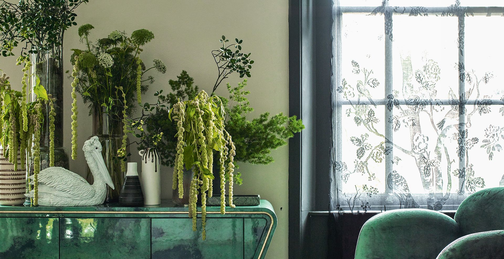 sage green living room with green console table filled with plants and forest green painted window frames